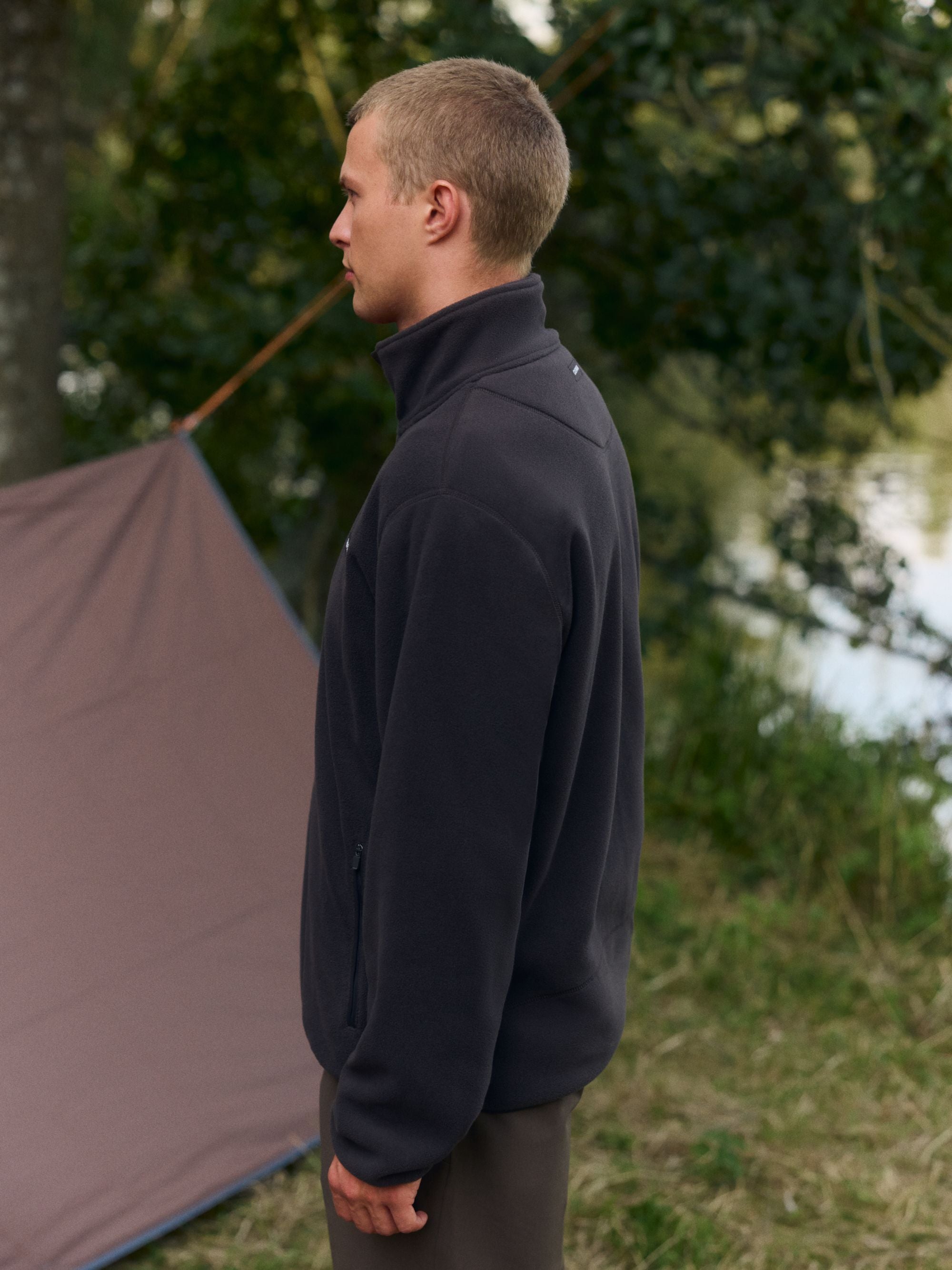 Man wearing a cocoa bean CASPARA polar fleece pullover outdoors next to a tent.